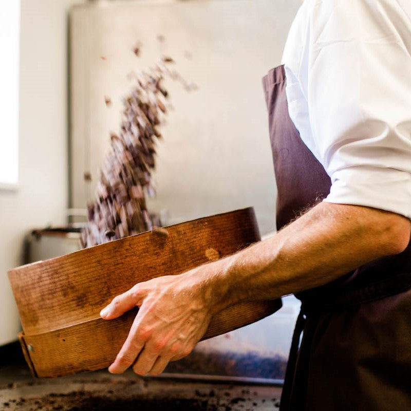 Unser Chocolatier siebt die Kakaobohnenstücke aus und bereitet alles für die Schokoladenherstellung vor.